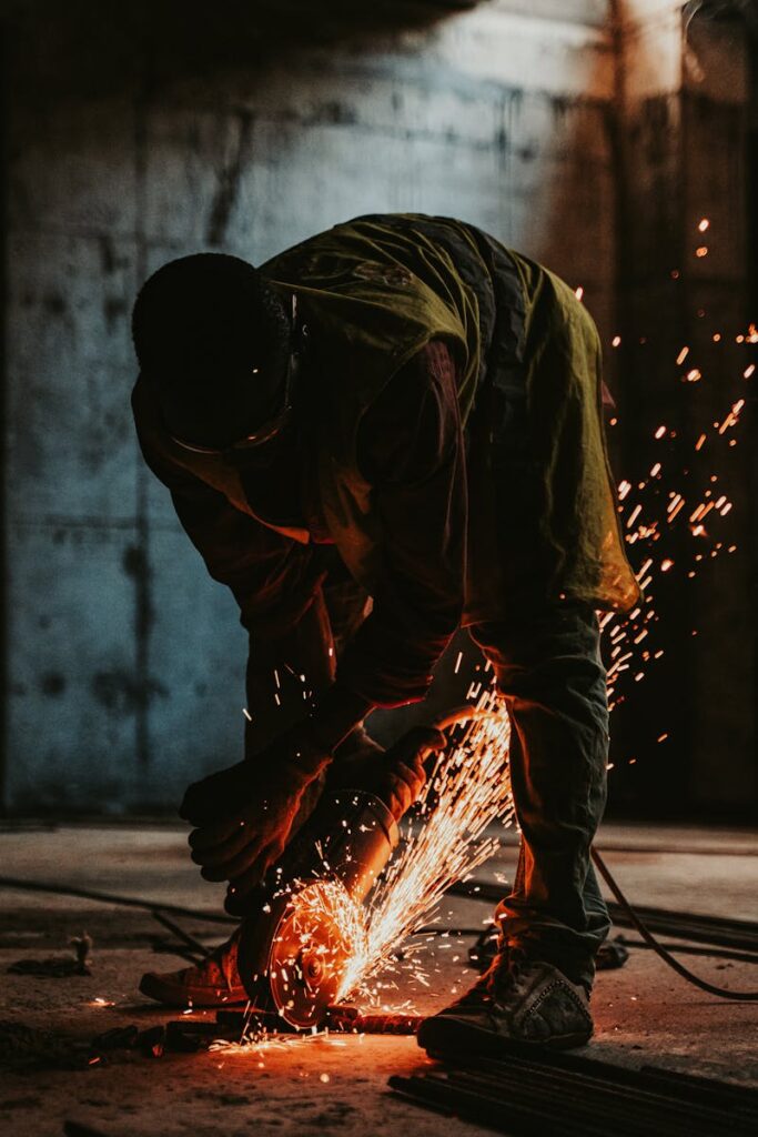 pexels-photo-19071946-19071946 Worker in silhouette cutting metal with sparks in a construction site at sunset.