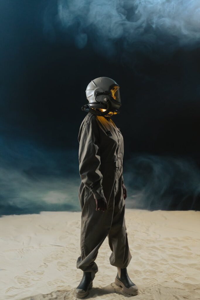 pexels-photo-7169854-7169854 Astronaut in space suit with helmet stands in foggy desert, side view against dark backdrop.